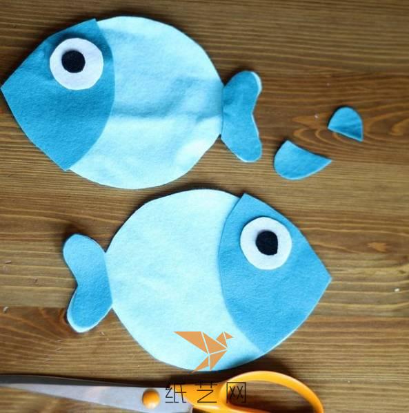 按照这两块不织布的大小，来剪出深蓝色的鱼脑袋和鱼鳍的部分，然后用白色和黑色的不织布来制作小鱼玩偶的眼睛